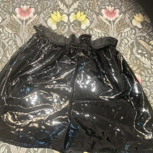 Svart glansig kjol från Flounce Club - Säljer en svart, glansig kortkjol från Flounce Club. Kjolen har resår i midjan och en riktigt cool wet look-finish som ger edgy vibes. Perfekt för dig som vill sticka ut och älskar statement-plagg. Passar till både chunky boots och sneakers.