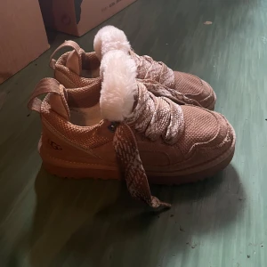Beige sneakers från UGG med teddyfoder - Chunky sneakers från UGG i beige mocka och textil med breda mönstrade snören och fluffigt vitt teddyfoder vid plösen. Snyggt vävd ovandel och grov sula ger en cool look. Perfekta för dig som vill ha både stil och komfort. Använda men så snygga syns inte så mycket