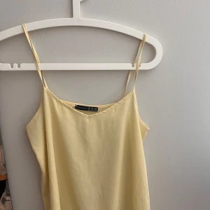 Ljusgul topp från Atmosphere -  Topp från Atmosphere med tunna axelband och enkel, rak passform. Perfekt för varma dagar med sitt luftiga tyg och minimalistiska stil. 
