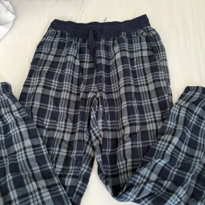 Blårutiga mjukisbyxor från Kappahl - Säljer ett par blårutiga mjukisbyxor från Kappahl i storlek 146/152. Byxorna har elastisk midja med snörning och är gjorda i mjukt bomullsmaterial. Perfekta för chill hemma eller häng med kompisar. Rutig design i mörkblå och grå toner.