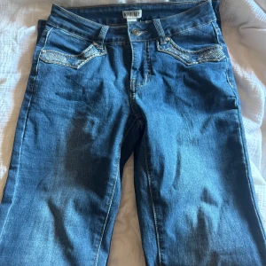 Blå jeans med broderade fickor Madlady - Snygga blå jeans från Madlady med coola broderade vingar på bakfickorna och glittriga detaljer. Klassisk fyrficksmodell med raka ben och normal passform. Perfekt för dig som vill sticka ut med lite extra detaljer. Byxorna är enbart testade. Säljer för 650kr och är i storlek 34 tall🤍