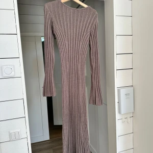 Beige ribbad långklänning från Adoore - Säljer en beige långklänning från Adoore med ribbad stickad struktur. Klänningen har långärmade ärmar med lätt utsvängda avslut och en rund halsringning. Modellen är figurnära och stretchig, perfekt för dig som gillar en slim passform.