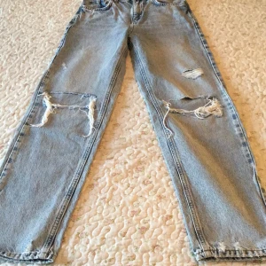 Ljusa ripped jeans från Gina Tricot - Säljer ett par ljusblå jeans från Gina Tricot med stora slitningar och hål på båda benen för en riktigt edgy vibe. Modellen är rak med klassiska fem fickor och hög midja. Perfekt för dig som gillar streetstyle och vill sticka ut. Längd från midjan: 96 cm. Midjan: 30 cm.