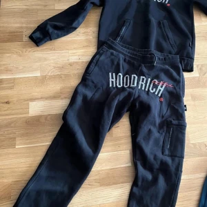 Svarta tracksuit från Hoodrich M lite använda men inte så mycket - Svarta byxor och tröja från Hoodrich med broderad logga framtill och coola detaljer. Byxorna har resår i midjan med snörning, sidofickor och en extra ficka på benet. Perfekta för en avslappnad streetwear-look.