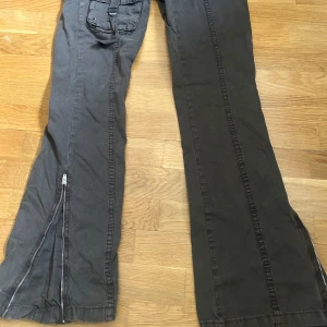 Bruna bootcut cargopants från BDG XS - Säljer ett par bruna cargopants från BDG Urban Outfitters i storlek XS. Byxorna har bootcut passform, flera fickor med lock och detaljer, dragkedjor vid bensluten och är gjorda av bomull med återvunnen bomull. Snygga sömmar längs benen och cool utility-vibe.