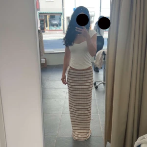 Randig långkjol i beige och vit - Säljer en snygg långkjol med horisontella ränder i beige och vitt. Kjolen har en tight passform och är stickad, vilket ger en mjuk och skön känsla. Perfekt för dig som gillar en enkel men trendig stil.