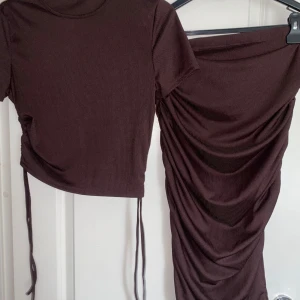 Brun croppad topp och kjol med snörning - Säljer mitt bruna ribbade set. En croppad kortärmad topp snörning i sidorna och en matchande kjol. 