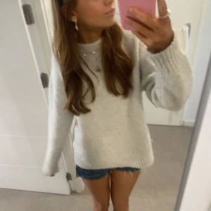 Vit stickad tröja från Zara - Mysig ljusgrå stickad tröja från Zara med ribbad hals, muddar och nederkant. Tröjan har en enkel, clean design och är perfekt för att hålla värmen under kyliga dagar. Passar dig som gillar en avslappnad och stilren look. Den är nopprig 