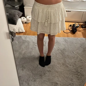 Vit kortkjol med volanger och snörning - Supersöt vit kortkjol med volanger och guldfärgade prickar. Kjolen kan justeras i midjan.