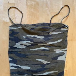 Camo linnetopp från Gina Tricot XS - Säljer en camouflagemönstrad linnetopp från Gina Tricot i storlek XS. Toppen har tunna axelband och är i mjuk bomullsmix. Färgerna går i mörkgrön, beige och svart, perfekt för dig som gillar streetstyle och vill sticka ut med coola mönster.
