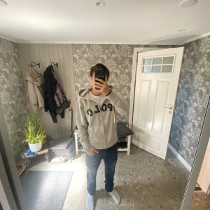 Grå hoodie från Polo Ralph Lauren - Säljer en grå hoodie från Polo Ralph Lauren med stor blå POLO-text på bröstet. Tröjan har dragkedja, huva med snörning och två fickor framtill. Materialet är mjuk bomull och polyester, perfekt för chill dagar. Klassisk och stilren look. Texten är lite sliten men det ser man på bilden. Den är i xs/s