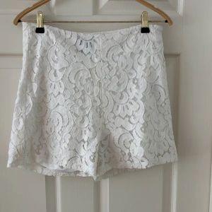 Vita spetsiga shorts med blommönster från Lindex  - Superfina vita shorts med blommig spets och fodrad insida. De har en feminin look med hög midja och är perfekta för varma dagar. Spetsen ger shortsen en romantisk vibe och de är lätta att matcha med både enkla och dressade toppar.