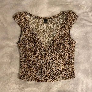 Leopardmönstrad croppad topp från SHEIN - Säljer en croppad topp från SHEIN med leopardmönster i beige, brunt och svart. Toppen är ärmlös med djup v-ringning och har en tight passform. Använd typ 5 gånger 