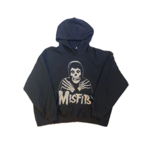 Svart Misfits hoodie Divided L - Svart hoodie från Divided med stort Misfits-tryck framtill och skelettmotiv. Klassisk huva och rymlig passform, perfekt för dig som gillar bandmerch och streetstyle. Tillverkad i mjuk bomullsmix för extra komfort.