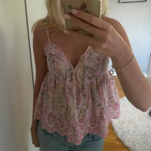 Rosa blommig linnetopp från BikBok - Supersöt rosa linnetopp från BikBok med blommigt mönster i grönt, vitt och gult. Toppen har smala axelband, v-ringning och broderade volangdetaljer längst ner. Perfekt för en somrig look och riktigt skön passform.