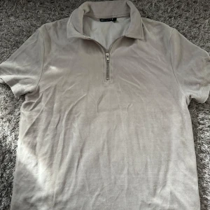 Grå pikétröja med half zip från ASOS - Snygg grå pikétröja från ASOS DESIGN i mjuk bomull. Tröjan har korta ärmar, klassisk krage och en trendig half zip-dragkedja framtill. Perfekt för dig som gillar en clean och stilren look med en twist.