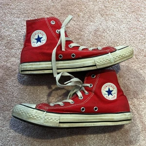 Röda Converse All Star high-tops (22cm) - ❤️‍🔥💸Klassiska röda Converse All Star high-tops med vit sula och tå, vita snören och tydliga loggor på sidan och hälen. Skorna har rund tå, platt sula och är tillverkade i canvas. Perfekta för en cool och avslappnad streetstil. De är flitigt använda, något som man ser på de vita delarna som har gulnat/mörknat en del, smuts. Men ändå något som kan bidra till den ”slitna/vintage o laidback” stilen. Perfekt nu till hösten💸❤️‍🔥