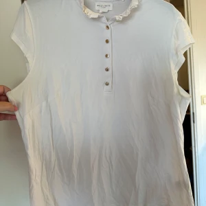 Vit blus med volangkrage Holly & Whyte strl: XL - Säljer en vit blus från Holly & Whyte med söt volangkrage och fem knappar framtill. Blusen är ärmlös och har en mjuk, lätt bomullskänsla. Perfekt för dig som gillar stilrena och feminina detaljer.