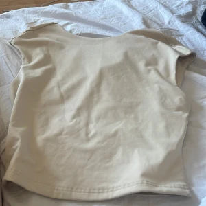 Beige croppad topp från SHEIN - Snygg beige croppad topp från SHEIN med rund hals och breda axlar. Den har även öppen rygg. Tillverkad i mjukt stretchigt material med 94% polyester och 6% elastan. Enkel och stilren design som är lätt att matcha med dina favoritjeans eller kjol.