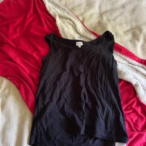Svart ärmlös linnetopp från Amalia - Enkel och stilren svart linnetopp från Amalia i storlek S. Toppen är ärmlös med rundad halsringning och tillverkad i mjuk bomull, perfekt att matcha med jeans eller kjol för en clean look.
