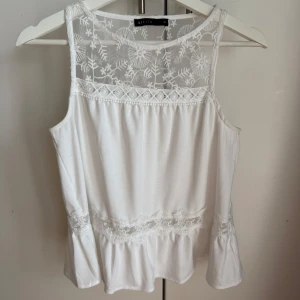 Vit spetsdetaljerad linnetopp Mohito - Supersöt vit linnetopp från Mohito med broderade spetsdetaljer upptill och längs nederkanten. Toppen är ärmlös och har en luftig, flowy passform. Perfekt för varma dagar när du vill ha något både romantiskt och stilrent. Materialet är 100% polyester. Storlek XS motsvarar S 