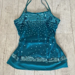 Turkos paljettopp Marks & Spencer - Supersnygg turkos linnetopp från Marks & Spencer med justerbara smala axelband. Toppen är täckt med glittriga paljetter framtill och har ett glansigt tyg som ger en festlig känsla. Perfekt för dig som vill sticka ut med lite extra bling! Passar mig som har storlek xs-s