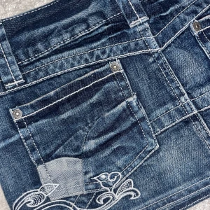 Jeanskjol med broderi från ONLY - Mörkblå jeanskjol från ONLY med snygga vita broderier av blommor och fågel framtill. Klassisk femficksmodell, bälteshällor och kontrastsömmar. Kort modell, inga defekter 💞