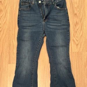Mörkblå bootcut jeans med hög midja - Snygga mörkblå jeans med bootcut och hög midja. Jeansen har klassisk femficksdesign, dragkedja och knapp framtill. Materialet är stretchigt denim som sitter skönt och formar sig efter kroppen. Perfekta för en trendig och avslappnad look.