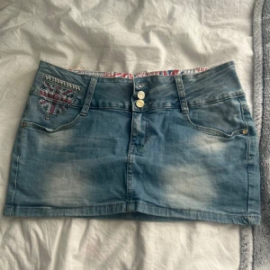 Blå jeanskjol  - Snygg kort jeanskjol från Miss Curry i ljusblå denim med två knappar fram.  Storlek 27/28.
