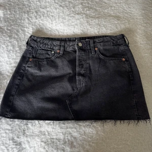 Svart jeanskjol från &Denim, S - Cool svart jeanskjol från &Denim i storlek S. Kjolen har klassisk design, knapp och dragkedja framtill, fransig kant nedtill. Säljer då den var för stor för mig, storleken är S men tycker den passar M också