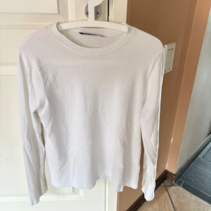 Vit långärmad tröja från Zara - Klassisk vit långärmad tröja från Zara i mjuk bomull. Enkel och stilren design med rund halsringning och ribbade detaljer vid halsen. Perfekt att matcha med jeans eller kjol för en clean look.