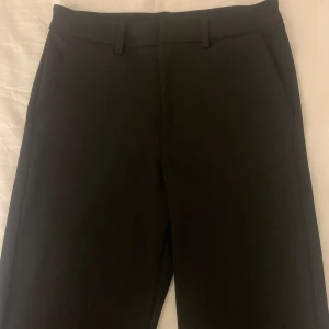 Svarta kostymbyxor från Kappahl - Klassiska svarta kostymbyxor från Kappahl i storlek 158. Byxorna har raka ben, hällor för bälte och sidfickor. Perfekta för en clean och stilren look. Materialet känns mjukt och följsamt.