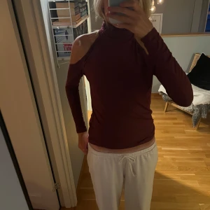 Vinröd polotröja med öppna axlar från Bik Bok - Säljer en vinröd polotröja från Bik Bok i mjuk bomull. Tröjan har lång ärm och cool offshoulder-design med öppna axlar. Passformen är slim och tyget är tunt och stretchigt, perfekt för att styla med jeans eller kjol. Polokrage ger en snygg touch.