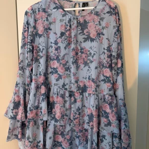 Blommig volangklänning från Vero Moda - Supersöt blommig klänning från Vero Moda i ljusblått. Kom tyvärr aldrig till användning så klänningen är helt ny men har missat returfönstret.