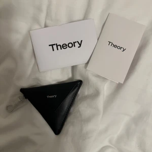 Svart trekantig plånbok från Theory - Minimalistisk svart plånbok från Theory i unik trekantig form. Perfekt för mynt eller småsaker när du vill ha något stilrent och annorlunda