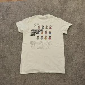 Drake Certified Lover Boy t-shirt vit - Vit t-shirt med tryck på ryggen från Drake och Certified Lover Boy. Trycket har coola emojis och låtlista i svart text. Klassisk rund hals och korta ärmar, tillverkad i mjuk bomull. Perfekt för dig som gillar musik och streetwear.