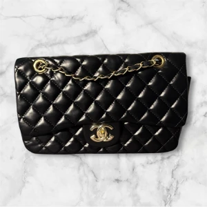 Svart quiltad Chanel handväska i skinn - Ikonisk svart handväska från Chanel med quiltad design och guldfärgad kedja. Väskan har klassiskt CC-spänne i guld och är tillverkad i mjukt skinn. Perfekt storlek för det viktigaste och har en snygg ficka på baksidan. En riktig statement piece för dig som gillar lyxiga detaljer.