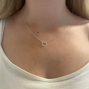 Sött halsband med hjärta i silver - Ett tunt och stilrent halsband i silver med ett öppet hjärta som hänge. Kedjan är finlänkad och ger ett minimalistiskt intryck, perfekt för dig som gillar enkla men snygga smycken. 