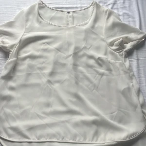 Vit blus med rund hals - Säljer en stilren vit blus med rundad hals och korta ärmar. Blusen har en lätt och flowy känsla, perfekt för dig som gillar en enkel men chic look. Materialet är mjukt och har en lätt glans, vilket ger en fräsch vibe. Passar dig som vill ha en clean och klassisk topp.