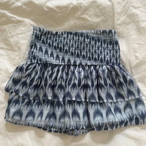 Blå mönstrad volangkjol - Supersöt kort kjol med blått och vitt mönster, bred smock i midjan och dubbla volanger. Den är i barnstorlek 146/152🥰 bara andvänd 1 gång!