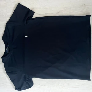  Polo Ralph Lauren T-shirt - Svart t-shirt från Polo Ralph Lauren med klassisk rund hals och korta ärmar. På bröstet sitter den ikoniska vita Polo-loggan broderad. T-shirten är gjord i mjuk bomull och har en clean, stilren look som funkar till allt.