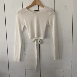 Vit ribbad croppad topp med knyt - Superfin vit långärmad topp med ribbad struktur och croppad passform. Toppen har snygg knytning i midjan som ger en trendig look. Perfekt att styla med höga jeans eller kjol. Mjukt och stretchigt material för skön känsla.