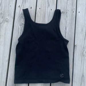 Svart ribbad tränings topp från Iconic - Svart ribbad tränings topp från Iconic i storlek 134/140. Toppen har breda axelband och ärmlös design, den är även kroppad och är gjord i ett mjukt bomulls material.