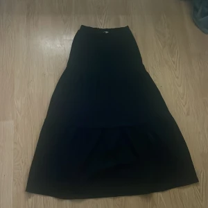 Svart långkjol från Samsa Young - Svart långkjol från Samsa Young i enkel och stilren design. Kjolen har en lätt utsvängd form och är helfärgad utan mönster eller detaljer. Perfekt för dig som gillar klassiska och tidlösa plagg. Passar dig som vill ha en basic kjol med mycket användningsmöjligheter.