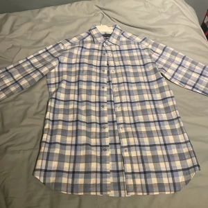 Rutig skjorta från Massimo Dutti - Säljer en stilren rutig skjorta från Massimo Dutti i blått och beige. Skjortan har långa ärmar och knappar framtill. Perfekt för en klassisk look.