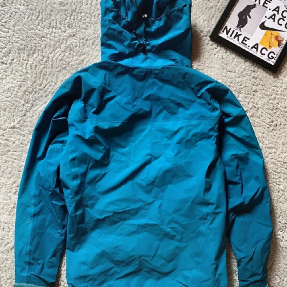 Säljer en blå vindjacka från Arc'teryx med huva och dragkedja. Jackan är tillverkad i Gore-Tex-material och har praktiska fickor med dragkedjor. Perfekt för utomhusaktiviteter och skyddar mot väder och vind. Pris går att diskutera, För fler bilder eller frågor så skriv till mig! . Takit.