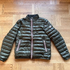 Moncler Daniel dunjacka - Snygg grön dunjacka från Moncler. I storlek 4 men den har krympt en del så nu passar den mer small eller medium. Fanns ett hål men det har blivit fixat av en professionell skräddare. (Se bild 4). Inget man märker från långt håll. Jackan är i allmänt bra skick men finns en del som skulle kunna fixas. Priset är ej hugget i sten🙏