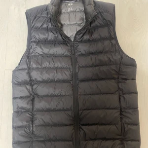 Svart dunväst från Uniqlo - Säljer en stilren svart dunväst från Uniqlo. Västen är ultralätt och har en dragkedja framtill. Perfekt för lager-på-lager under kyliga dagar.