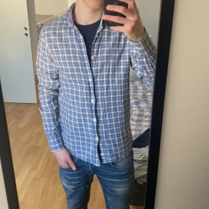 Rutig skjorta från Morris - Snygg rutig skjorta från Morris i blått och vitt med klassisk krage och knappar framtill. Perfekt för en stilren look. Skjortan har långa ärmar och är tillverkad i ett bekvämt material.