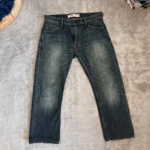 Levi’s 505 - Säljer ett par klassiska blå jeans från Levi's med en straight fit. De har en traditionell femficksdesign och en knappgylf. Perfekta för en avslappnad stil. Orginal längden har blivit klippt och har nu en längd på 64 cm. 